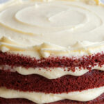 Homemade classic red velvet cake layered with rich cream cheese frosting on a cake stand.